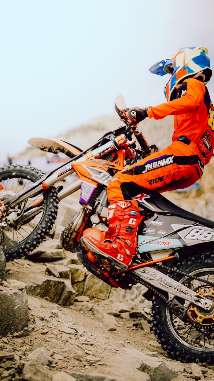 Motocross rider in vibrant gear navigating rocky terrain in Indonesia, showcasing skill and determination.